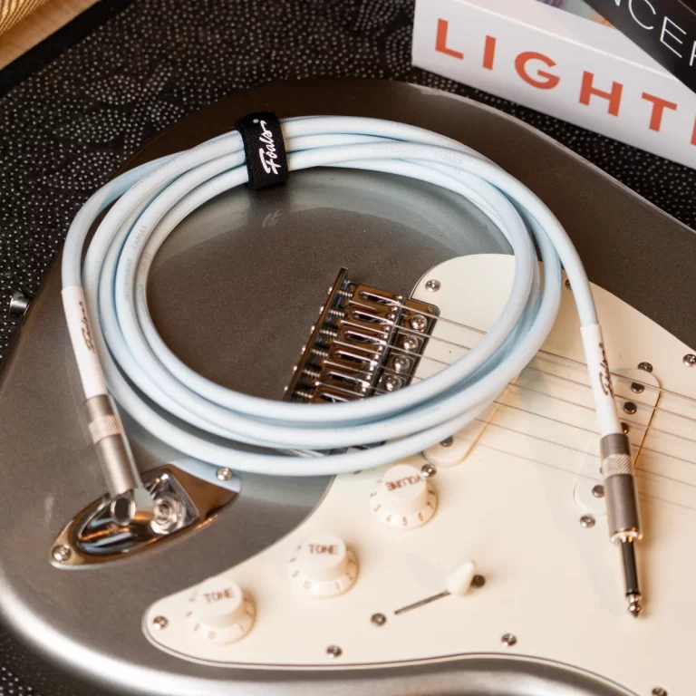 Electric guitar with a coiled light-blue instrument cable resting on its body, Fender-branded connector visible. ขายราคาพิเศษ
