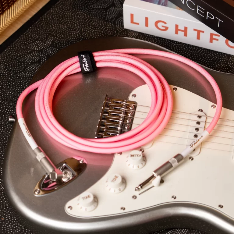 Silver electric guitar with a white pickguard and a bright pink coiled instrument cable laid across its body. ขายราคาพิเศษ