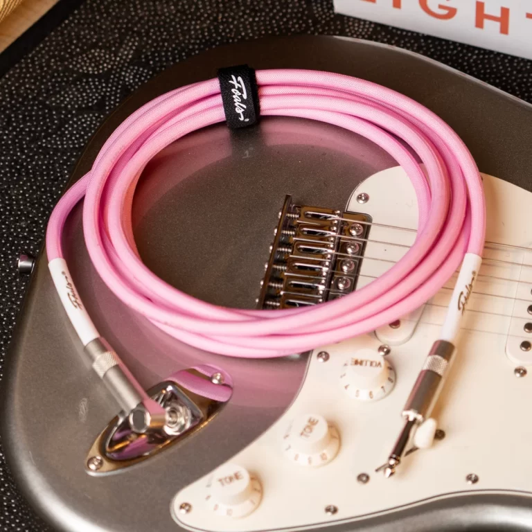 Coiled pink guitar cable resting on a Fender-style electric guitar with a white pickguard edge visible. ขายราคาพิเศษ