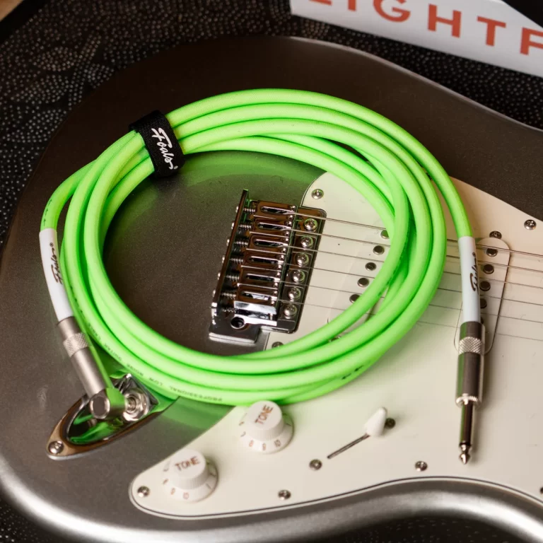 Bright neon green guitar cable coiled on a metallic gray electric guitar with a white pickguard and chrome bridge. ขายราคาพิเศษ