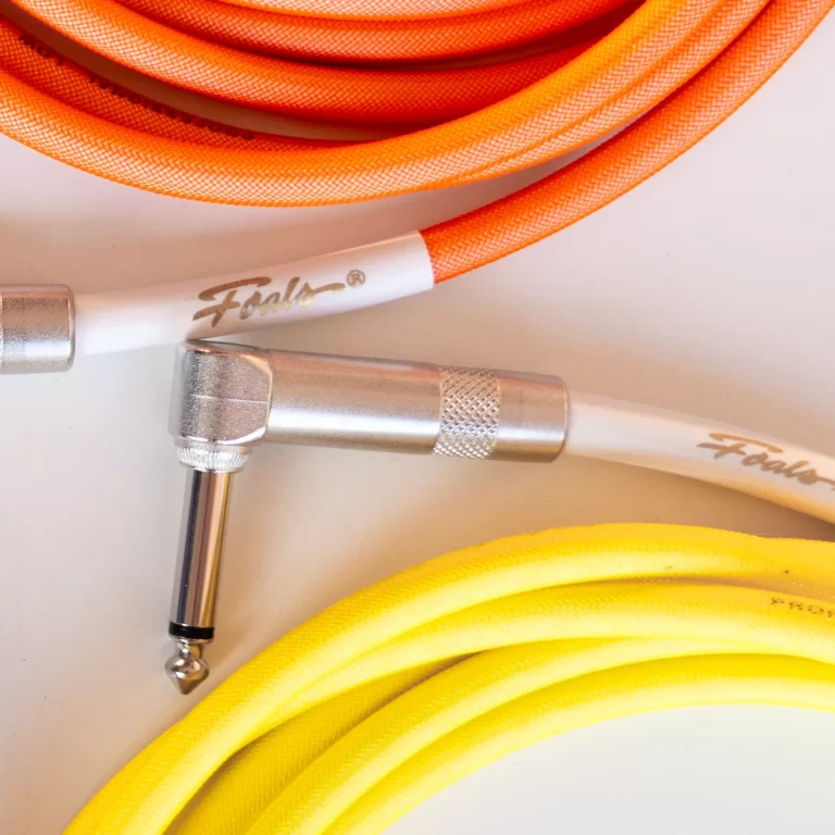 Coiled orange and yellow braided instrument cables with silver 1/4 inch plugs connected to metal jacks on a white background ขายราคาพิเศษ