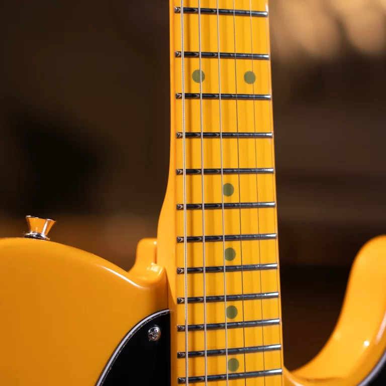 Close-up of a yellow electric guitar neck with frets, strings, and green dot inlays on the fretboard. ขายราคาพิเศษ
