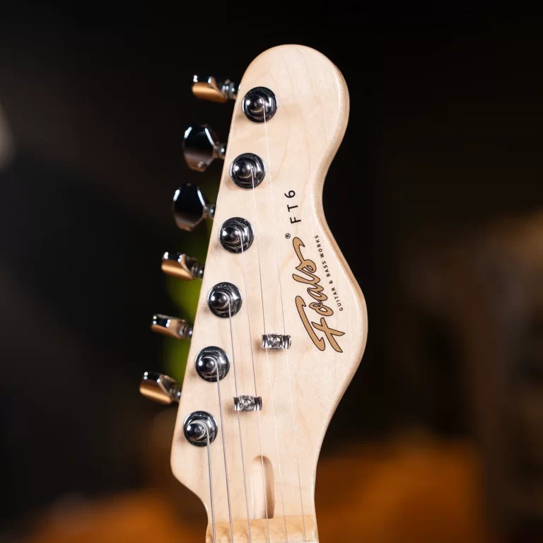 Close-up of a Fender guitar headstock with six chrome tuning pegs and strings running down the neck. ขายราคาพิเศษ