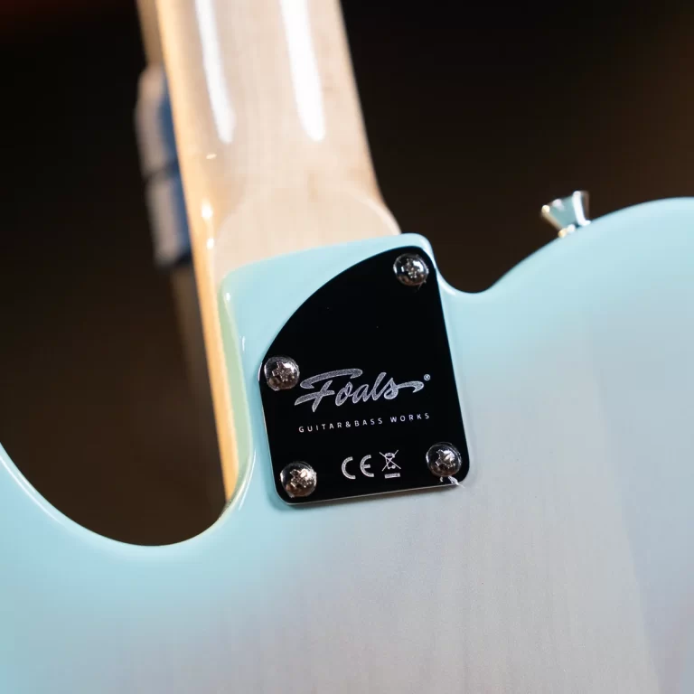 Brand plate on the back of a light blue electric guitar reading 'Foals Guitars & Bass Works' with screws visible at corners. ขายราคาพิเศษ
