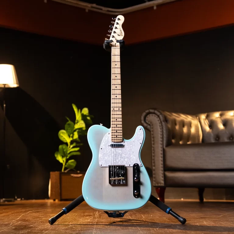 Light blue Fender Telecaster–style electric guitar on a stand in a dim living-room setup with a sofa in the background. ขายราคาพิเศษ
