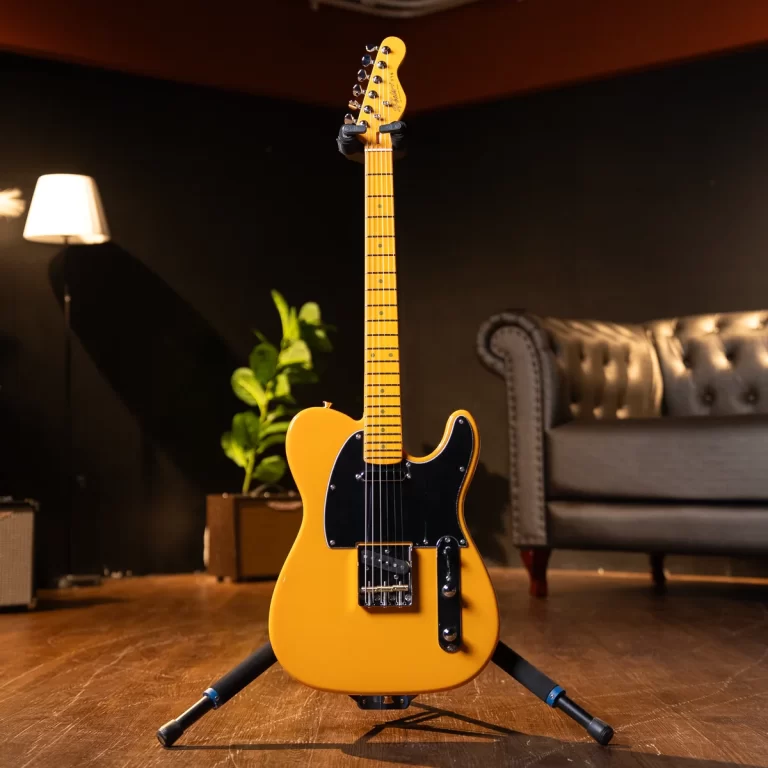 Yellow electric guitar on a floor stand in a cozy studio living room with a tufted sofa and plant in the background. ขายราคาพิเศษ