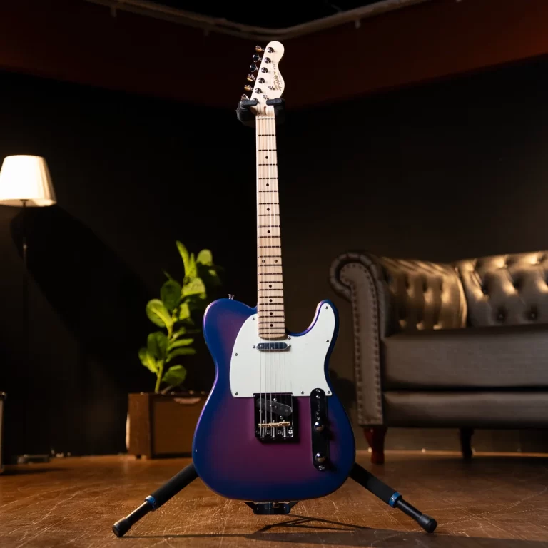 Blue-to-purple gradient Fender-style electric guitar on a stand in a cozy living-room studio with a lamp and sofa nearby. ขายราคาพิเศษ