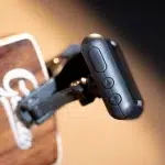 Close-up of a black action camera remote with three round buttons on its side, mounted on a strap. ขายราคาพิเศษ