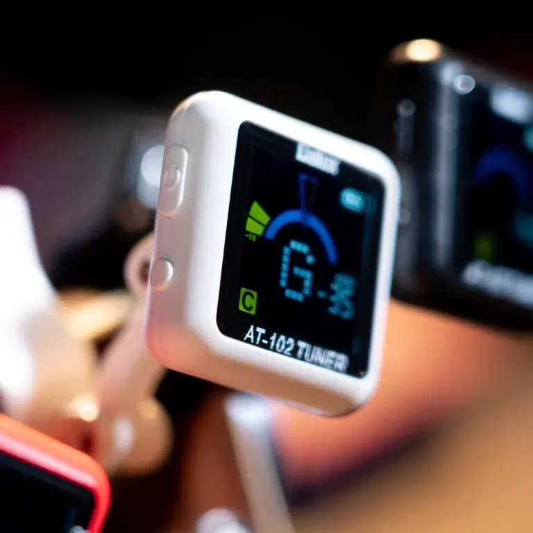 White clip-on tuner device with a digital display showing AT-102 TUNER, used for tuning musical instruments. ขายราคาพิเศษ