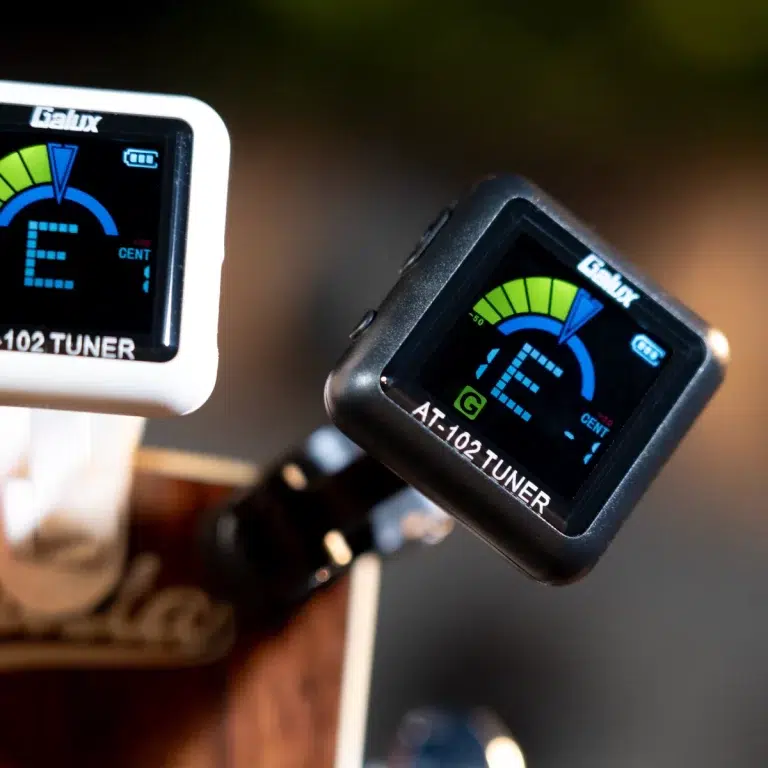 Close-up of two guitar tuner devices on a guitar neck, displaying bright digital tuning meters and notes (E and G). ขายราคาพิเศษ