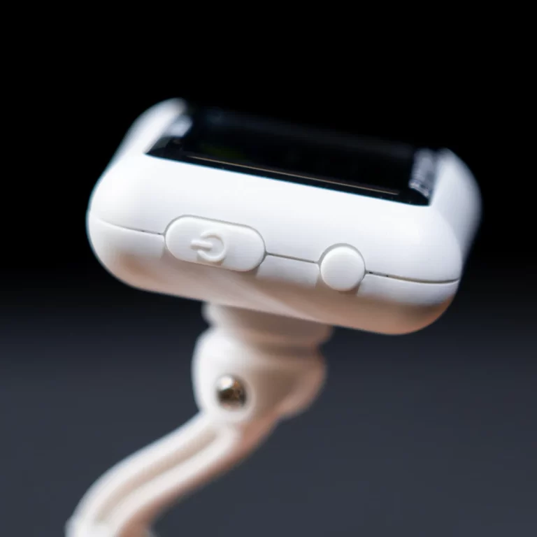 Close-up of a white pulse oximeter with a small screen, side power button, and attached strap against a dark background. ขายราคาพิเศษ
