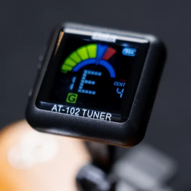 Electronic guitar tuner device displaying a colorful meter and digital readout, labeled AT-102 TUNER on the housing. ขายราคาพิเศษ