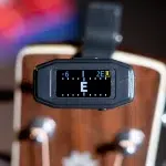 Guitar tuner clipped over the headstock showing note E with tuning markers on a black display. ขายราคาพิเศษ