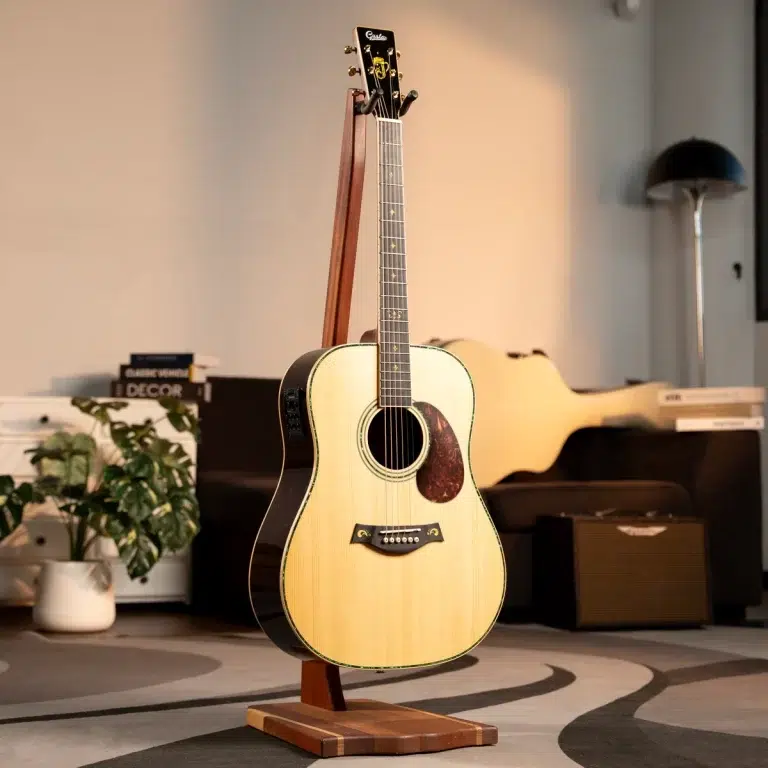 Acoustic guitar with light wood top on a wooden stand in a cozy living room, next to a plant and magazines on a low shelf. ขายราคาพิเศษ