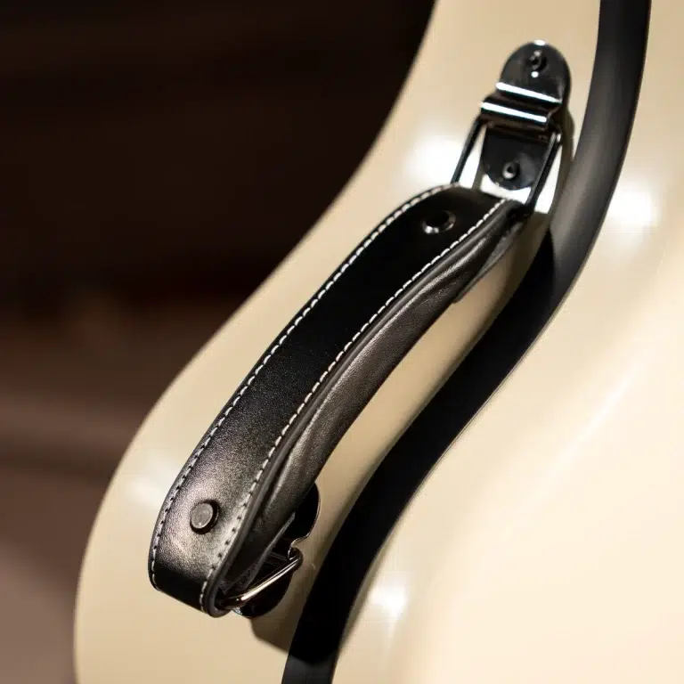 Close-up of a black leather guitar strap with white stitching attached to a cream-colored guitar body by a metal strap button. ขายราคาพิเศษ