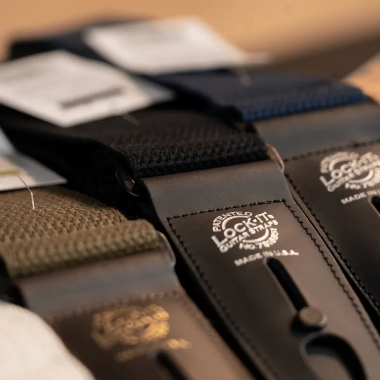 Close-up of a black leather guitar strap with fabric webbing and a Lock-It brand stamp. ขายราคาพิเศษ