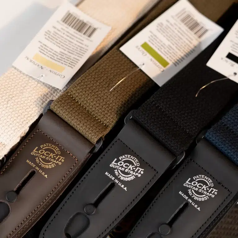 Close-up of three Lock It guitar straps with fabric straps in beige, brown, and black, showing leather ends and product tagsIN ขายราคาพิเศษ
