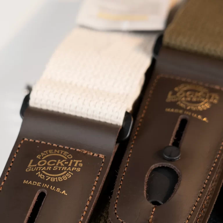 Close-up of brown leather guitar strap ends with a white woven strap and embossed 'Lock-It' logo. Made in USA text visible in gold., ขายราคาพิเศษ