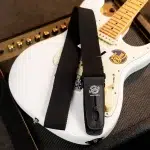 Close-up of a white electric guitar with a black strap and a strap-lock on the body. ขายราคาพิเศษ