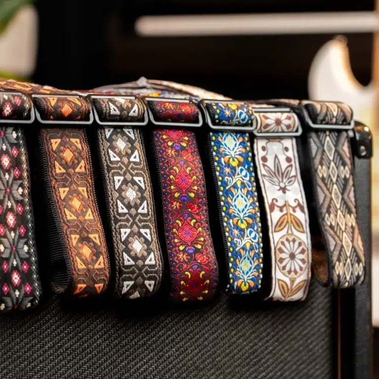 Colorful patterned guitar straps hanging along the edge of a black amplifier, showcasing intricate embroidery. ขายราคาพิเศษ