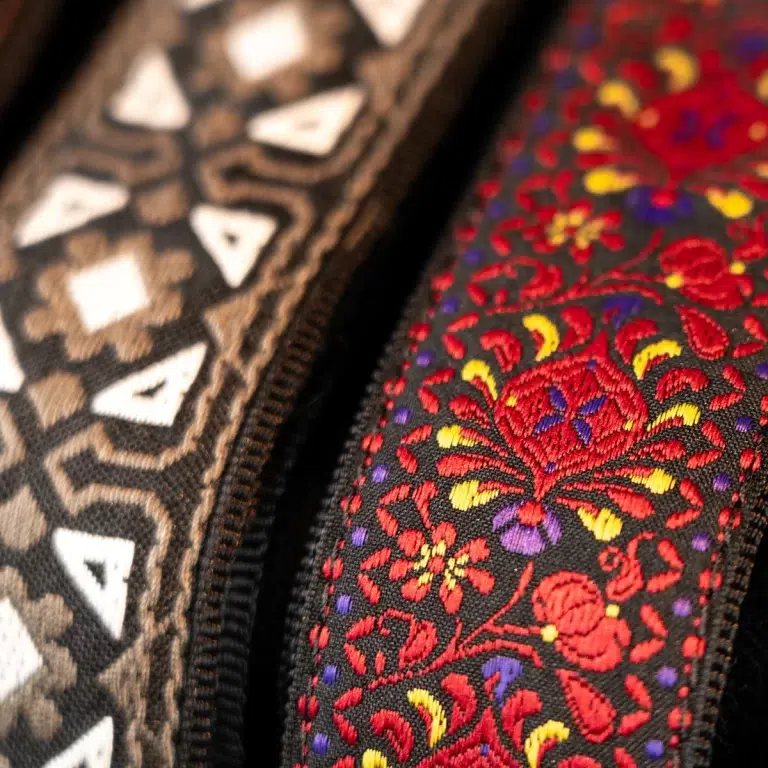 Close-up of two decorative zippers on patterned fabrics: a beige geometric design and a black fabric with colorful red floral embroidery. ขายราคาพิเศษ
