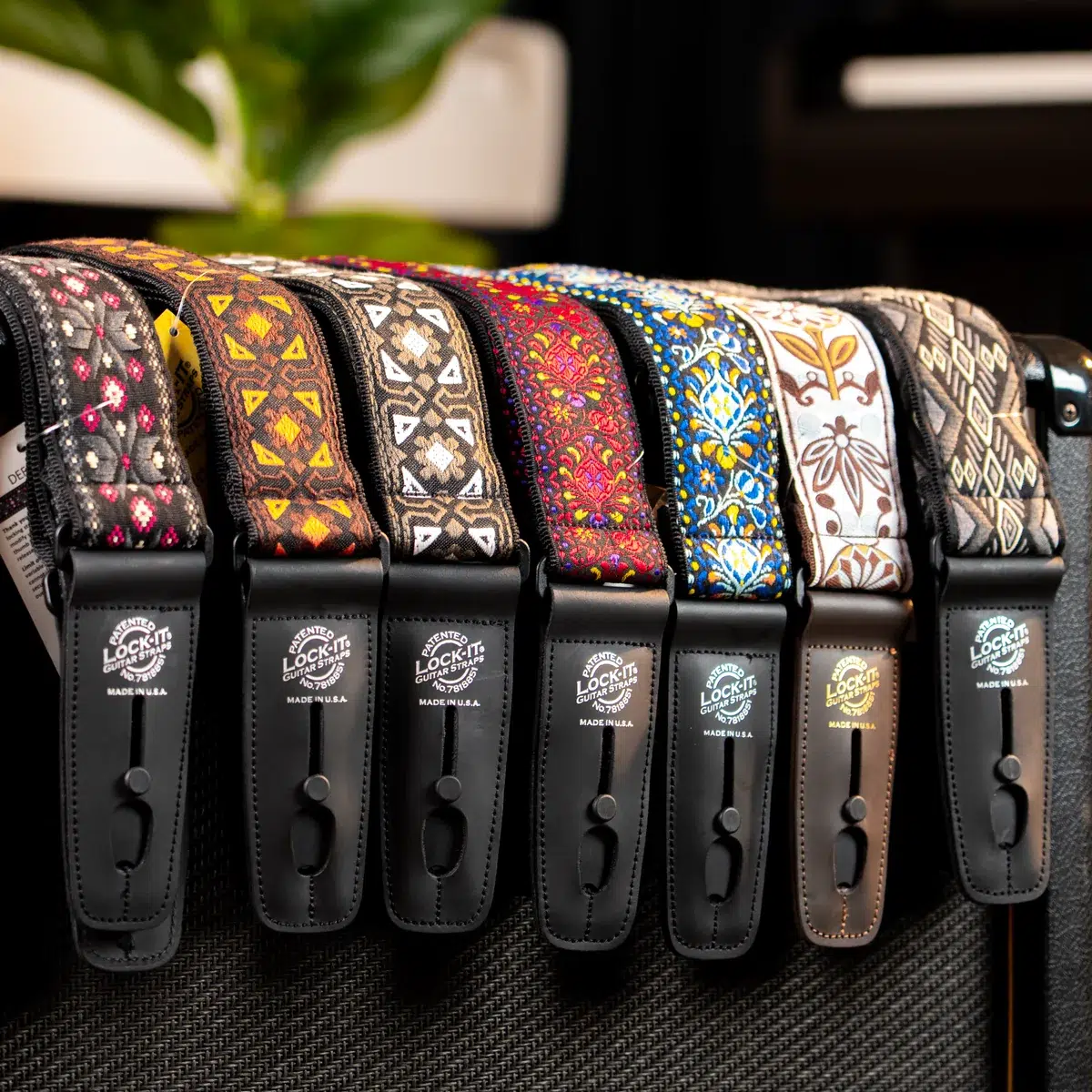 Row of colorful patterned guitar straps with black leather ends, hanging on a guitar amp on display.
