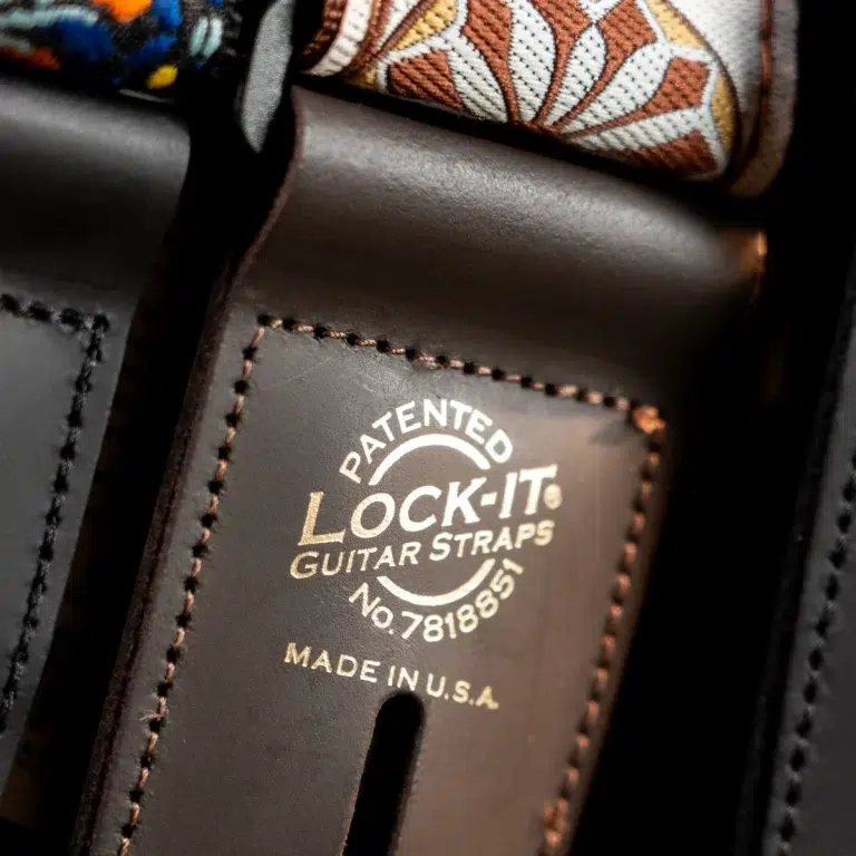 Close-up of a leather guitar strap with a stamped 'Patented Lock-It Guitar Straps' logo and 'Made in USA' text. ขายราคาพิเศษ