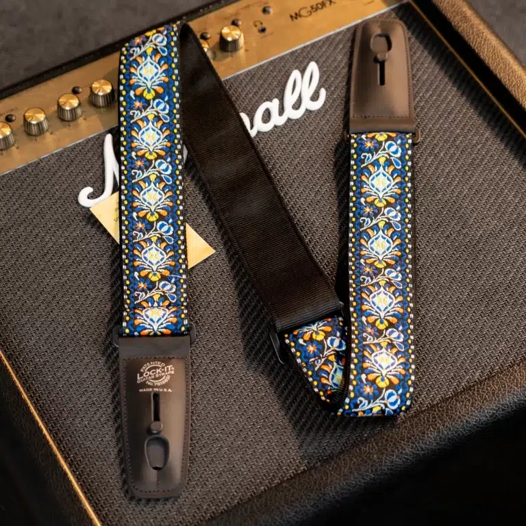Two decorative guitar straps with a blue, yellow, and white floral pattern and leather ends, resting on a guitar amplifier. ขายราคาพิเศษ