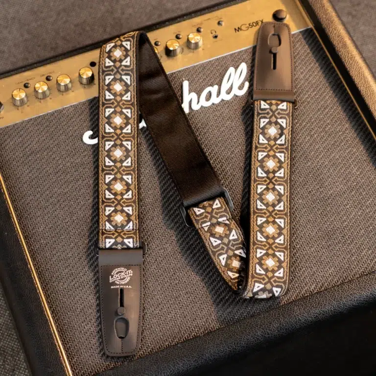 Patterned brown guitar strap laid across a vintage brown amplifier cabinet with textured grille cloth. ขายราคาพิเศษ