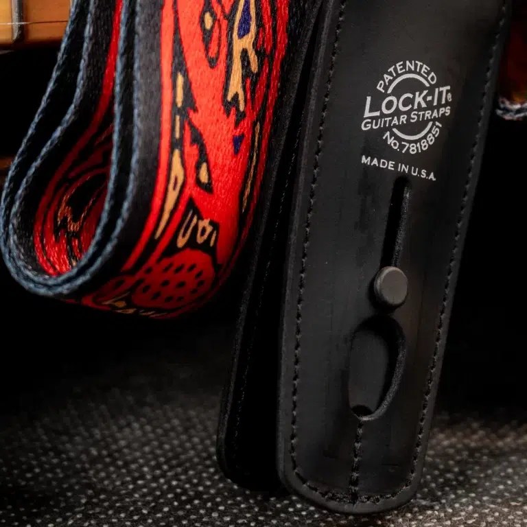 Close-up of a black leather guitar strap with a red patterned strap next to it, showing 'LOCK-IT GUITAR STRAPS' branding and 'Made in U.S.A.' ขายราคาพิเศษ