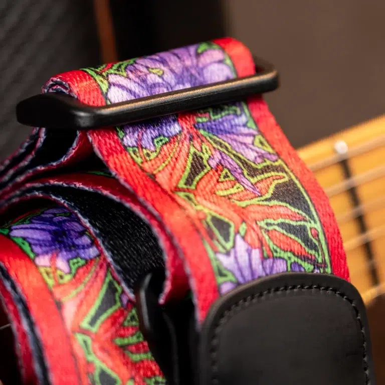 Close-up of a red and purple floral guitar strap attached to a guitar surface. ขายราคาพิเศษ