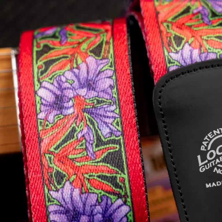 Close-up of a colorful floral guitar strap with red edges and purple flowers, attached to a wooden guitar. ขายราคาพิเศษ