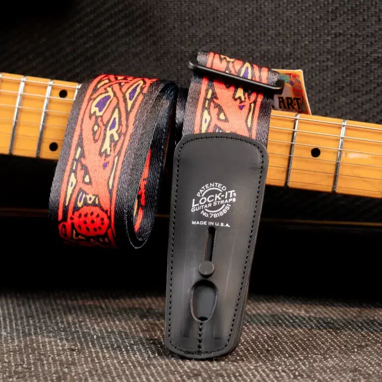 Patterned fabric guitar strap looped over a guitar neck with a black leather end that reads 'Lock-It Guitar Straps'. ขายราคาพิเศษ