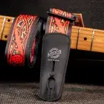 Close-up of a black leather Lock-It guitar strap lock attached to a colorful red-patterned strap resting on a guitar neck. ขายราคาพิเศษ