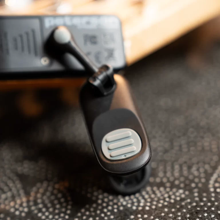 Close-up of a black handheld device with a gray circular button featuring three horizontal raised bars; blurred background gear/s equipment behind it. ขายราคาพิเศษ