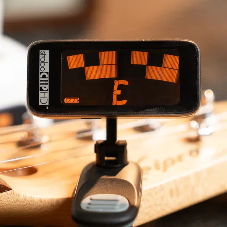 StrobeClipHD guitar tuner mounted on a stand with orange LED segments on a dark screen in the foreground. ขายราคาพิเศษ