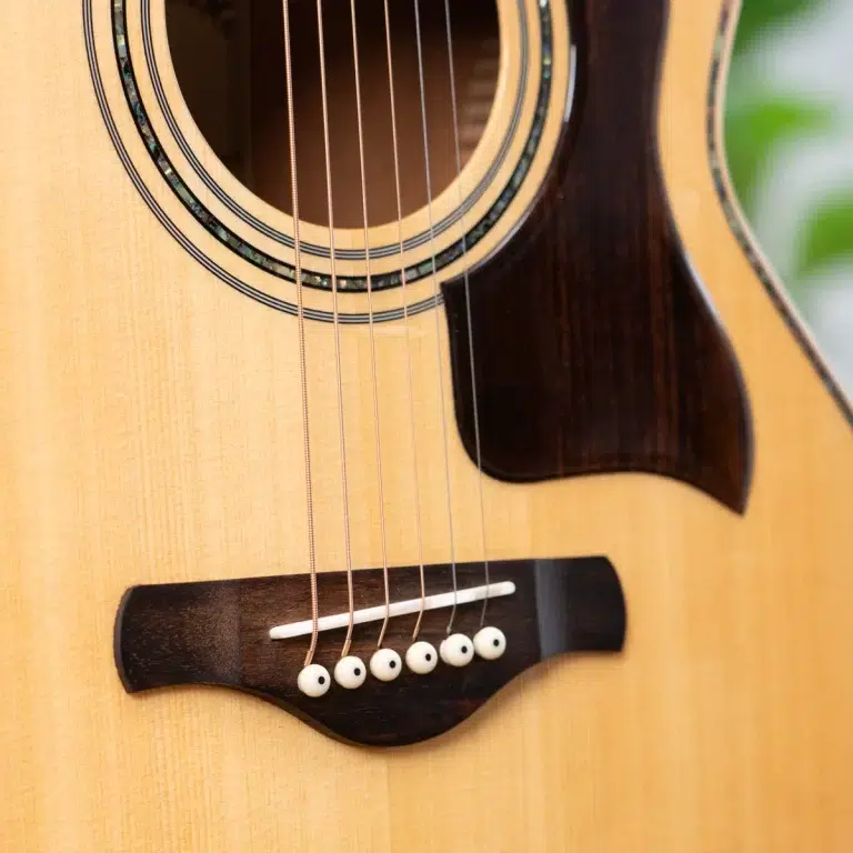 Close-up of an acoustic guitar showing the sound hole, strings, and wooden bridge with white bridge pins. ขายราคาพิเศษ