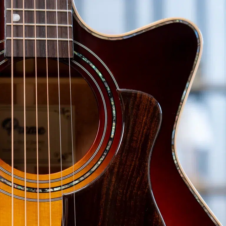 Close-up of an acoustic guitar showing strings over the soundhole and glossy wood finish ขายราคาพิเศษ