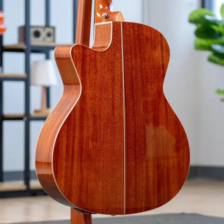 Back view of a polished wooden acoustic guitar standing on a stand indoors, showing its reddish-brown grain and rounded body edge. ขายราคาพิเศษ