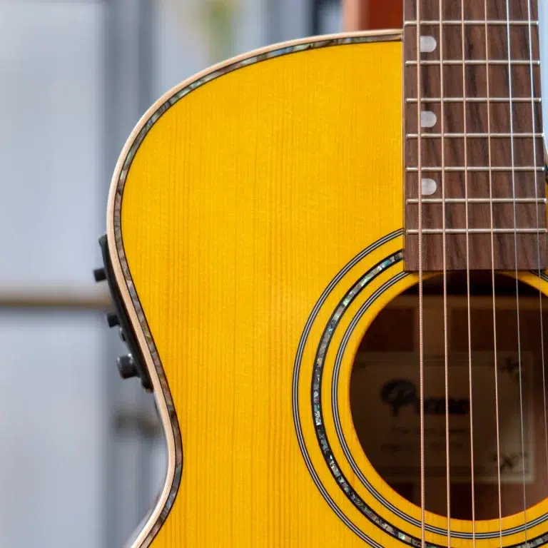 Close-up of a yellow acoustic guitar showing the soundhole, decorative rosette, and strings on the right side of the image. ขายราคาพิเศษ