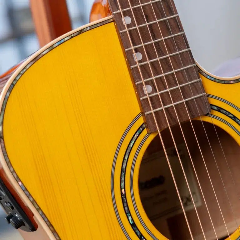 Close-up of a yellow acoustic guitar showing the body, strings, and fretboard with white dot inlays by the neck edge. ขายราคาพิเศษ