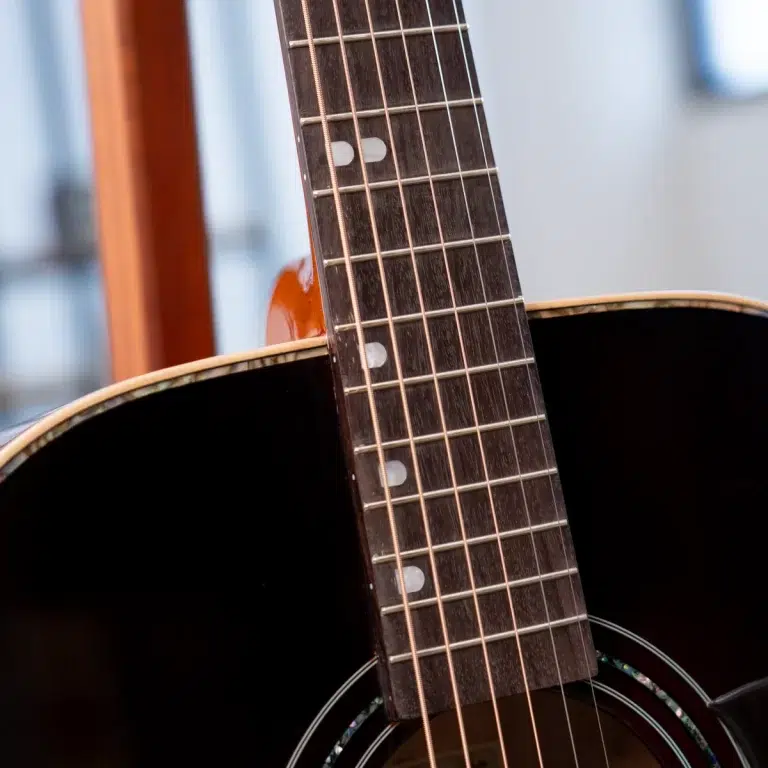Close-up of an acoustic guitar neck showing frets, strings, and fretboard in dark wood. ขายราคาพิเศษ