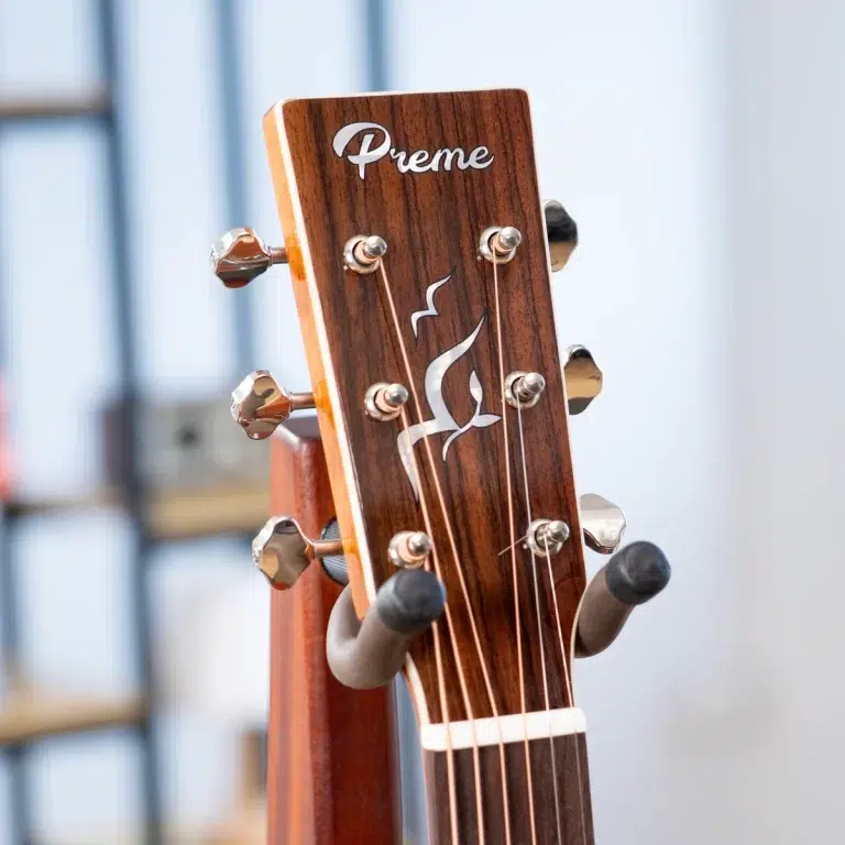 Close-up of a wooden guitar headstock with six tuning pegs and the brand name 'Preme' on it. ขายราคาพิเศษ
