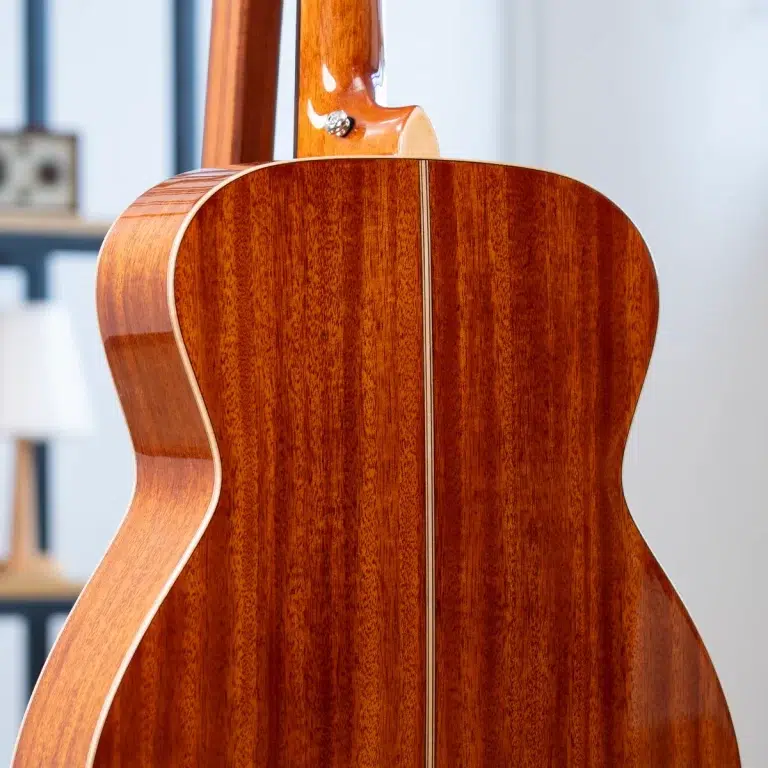 Back of a glossy wooden acoustic guitar with a light binding, showing the center seam and neck joint in a bright room. ขายราคาพิเศษ