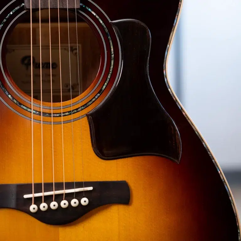 Close-up of an acoustic guitar showing the sound hole, rosette, and six steel strings over the sunburst body. ขายราคาพิเศษ