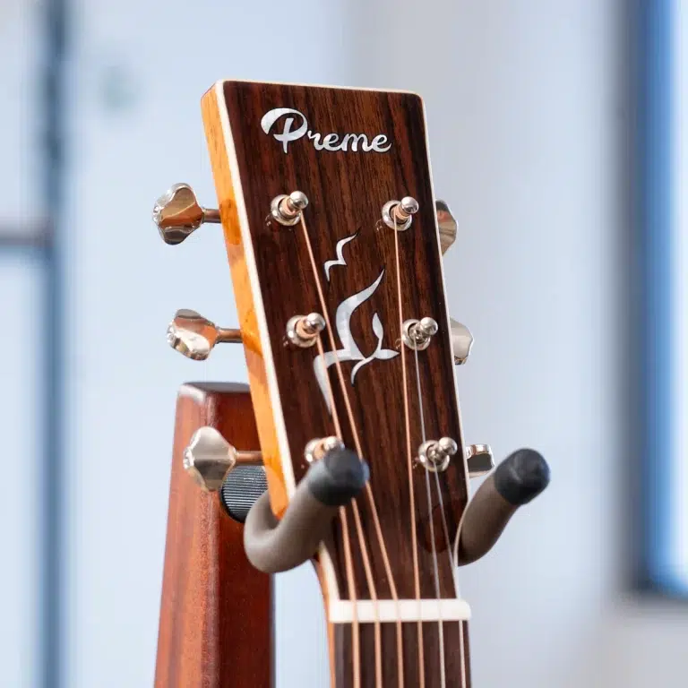 Close-up of a wooden guitar headstock with tuning pegs and a 'Preme' logo; strings run over the nut. ขายราคาพิเศษ