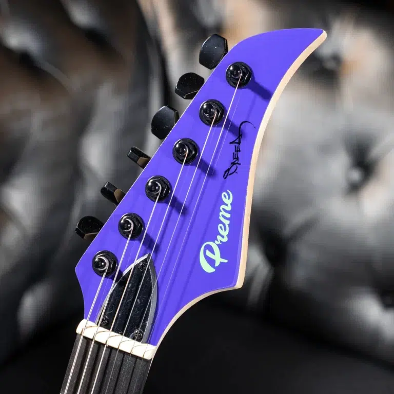 Close-up of a purple guitar headstock with six tuning pegs and strings, featuring a Dream logo on a blurred background. ขายราคาพิเศษ