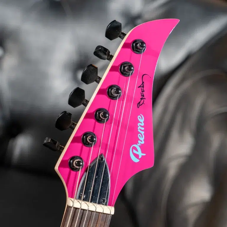 Close-up of a bright pink electric guitar headstock with six black tuning pegs and strings. ขายราคาพิเศษ