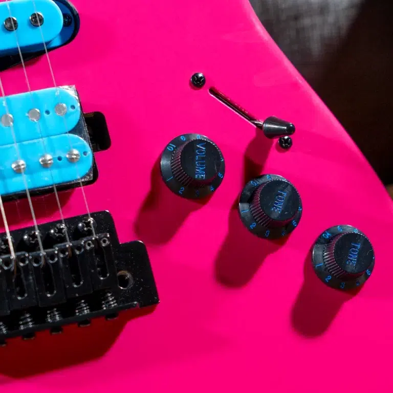 Close-up of a bright pink electric guitar showing volume and tone knobs, pickup, and bridge.