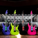 Four neon-colored electric guitars (blue, lime green, black, and pink) stand on a wooden floor in front of a tufted gray sofa. ลดราคาพิเศษ